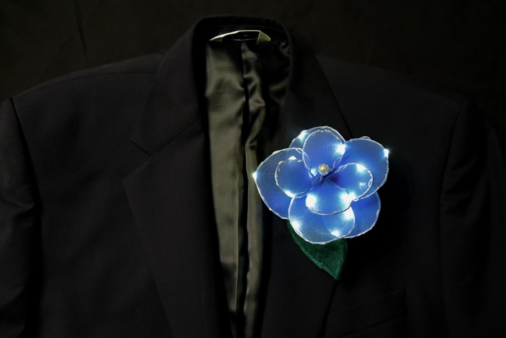 A blue, light-up boutonniere flower is pinned to the lapel of a sports jacket.