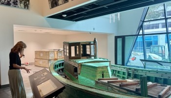 A woman stands at a display of a boat in a museum.