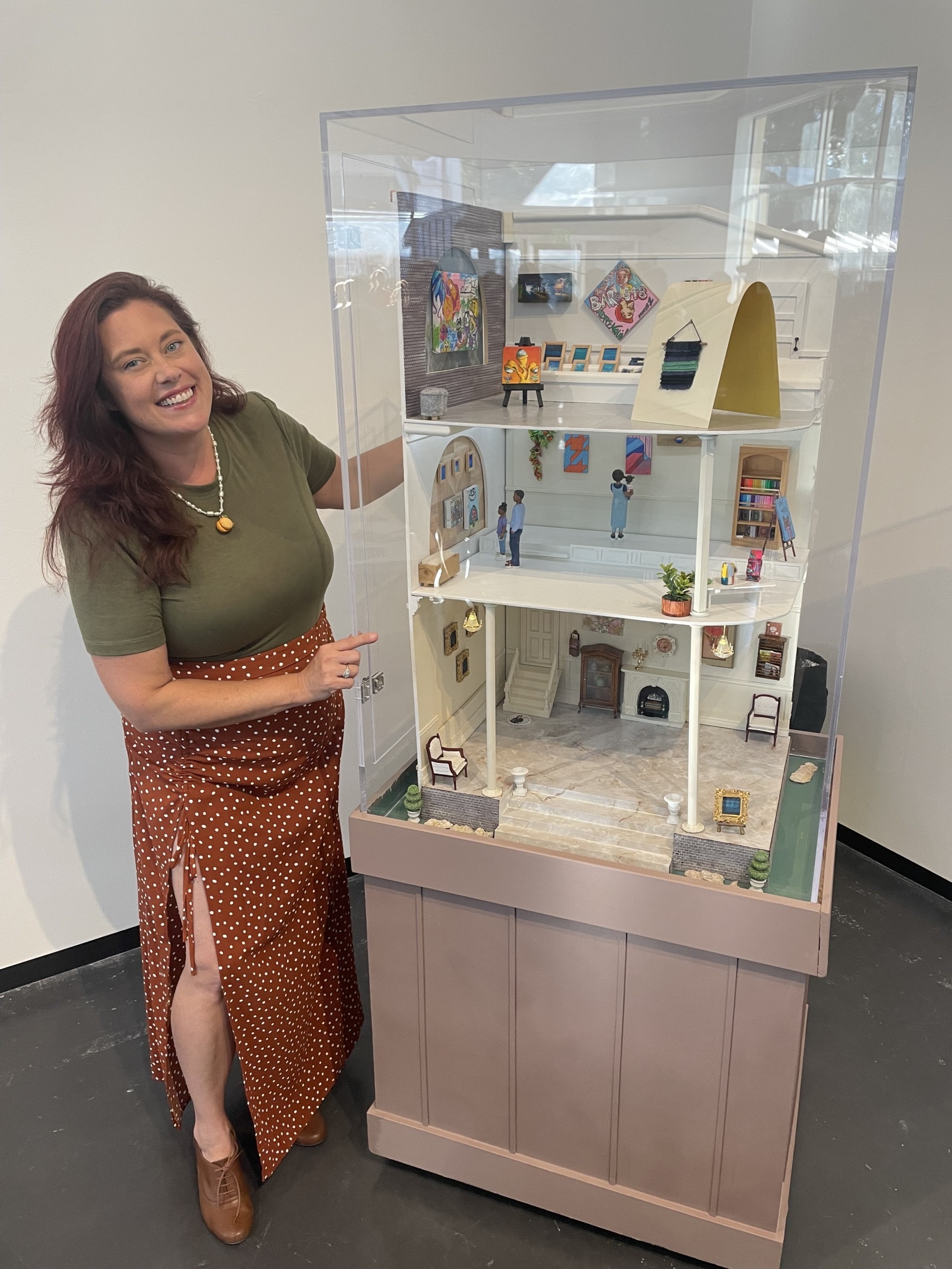 A woman poses with a dollhouse-like miniature art gallery.