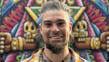 A man smiles in front of his colorful artwork.