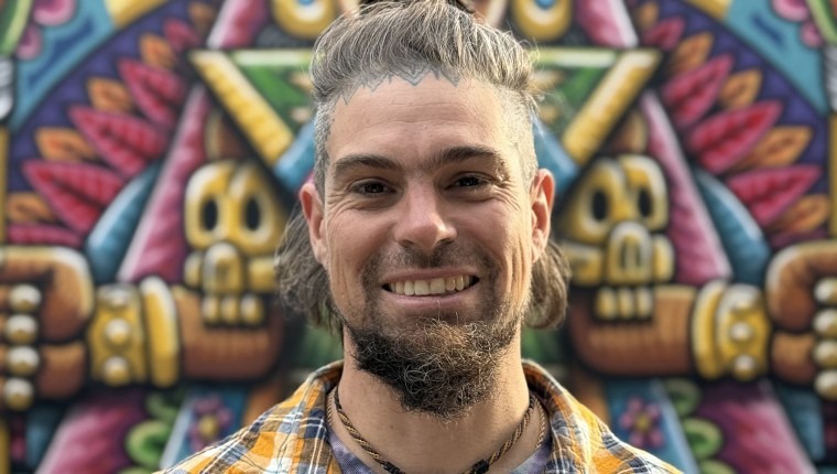 A man smiles in front of his colorful artwork.