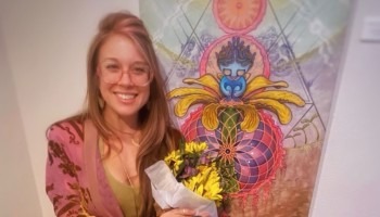 A woman smiles and holds flowers in front of a painting.
